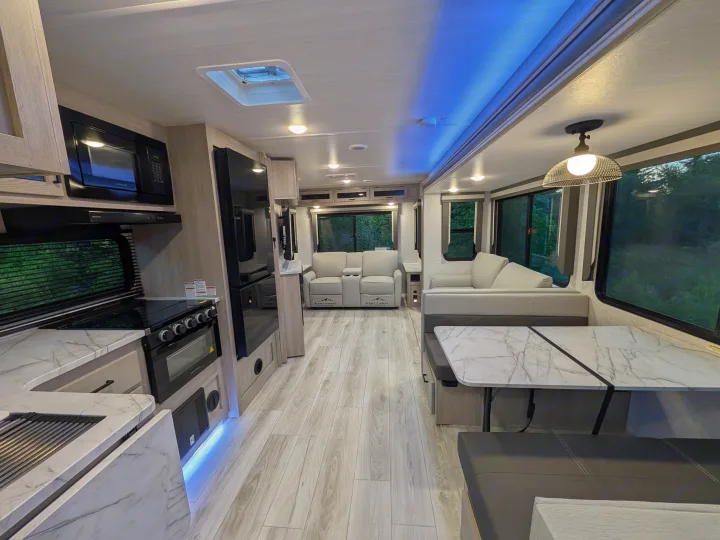 RV rental interior: modern kitchen with oven, microwave, marble counters; living area, comfy seating, wood floors, blue lights.. Forest River Alta 2850KRL 2025