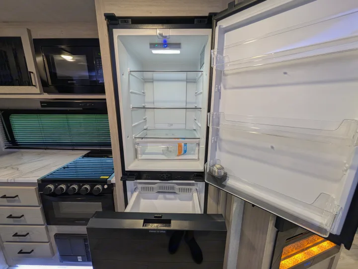 Inside an rv rental: a modern, open refrigerator in a compact kitchen with microwave, stove, and functional storage.. Forest River Alta 2850KRL 2025
