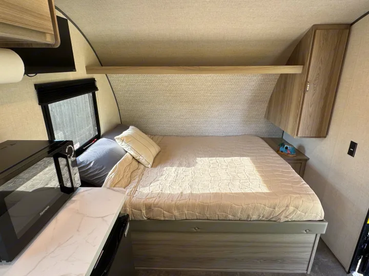 Cozy RV rental bedroom features a comfortable bed, overhead storage, and a handy microwave.. Forest River Wildwood FSX Platinum 2025