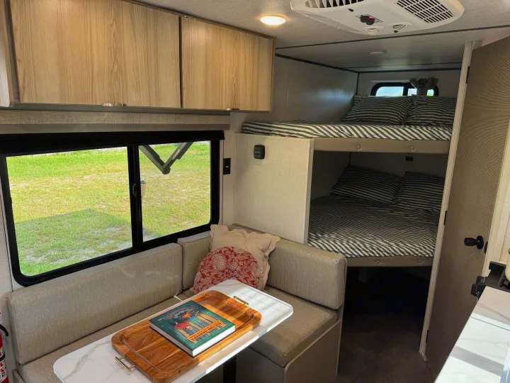 Cozy RV rental interior with dinette, large window, and comfy bunk beds. Ideal for family trips.. Forest River Wildwood FSX Platinum 2025
