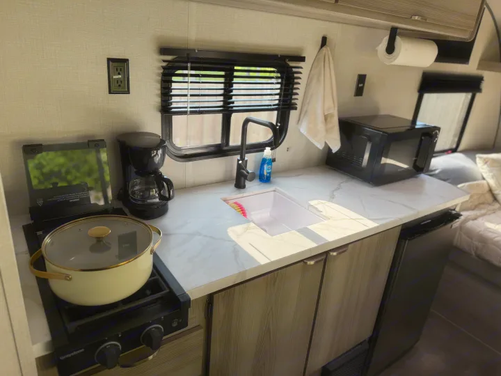 This modern RV rental kitchen has a sink, stove, coffee maker, and microwave, efficiently designed for travel cooking.. Forest River Wildwood FSX Platinum 2025