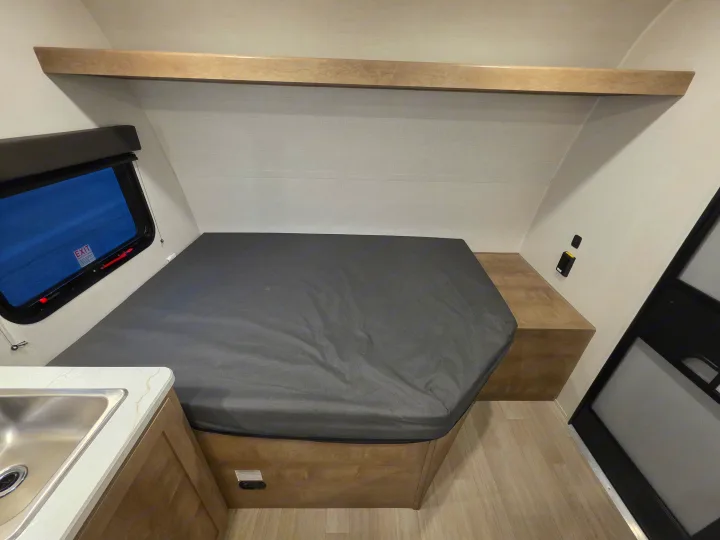 RV rental interior: A compact sleeping area with a grey bed, emergency exit window, and small sink. Ideal for road trips.. Keystone Springdale 2026