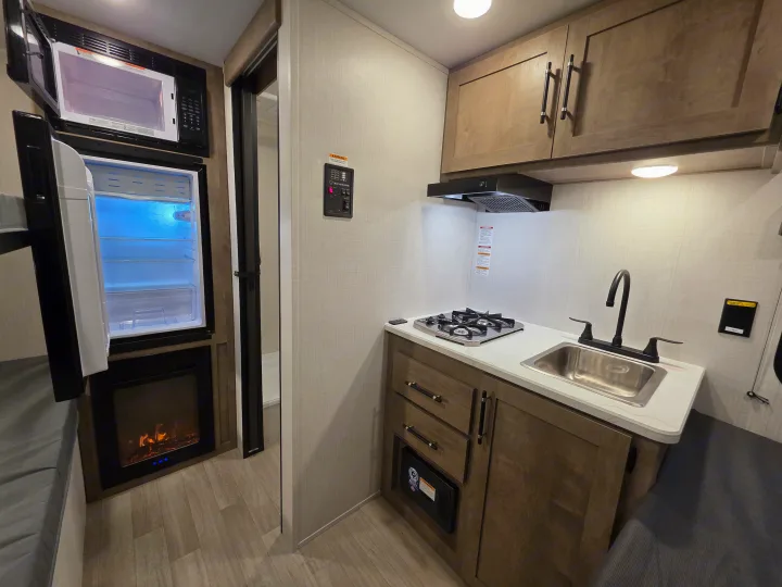 Cozy RV rental interior showcasing a well-equipped kitchenette with sink, cooktop, microwave, fridge, and electric fireplace.. Keystone Springdale 2026