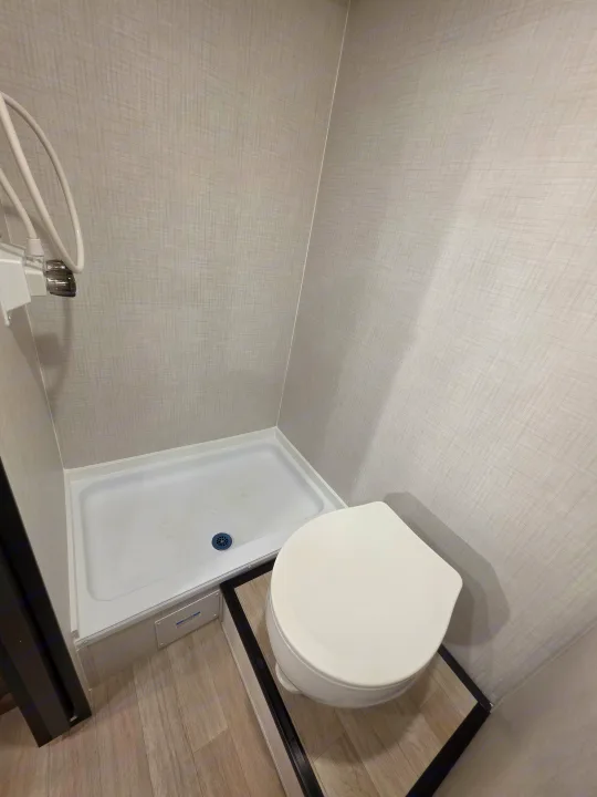 Compact RV rental bathroom featuring a white toilet, shower stall with white base, and light wood-look floor.. Keystone Springdale 2026