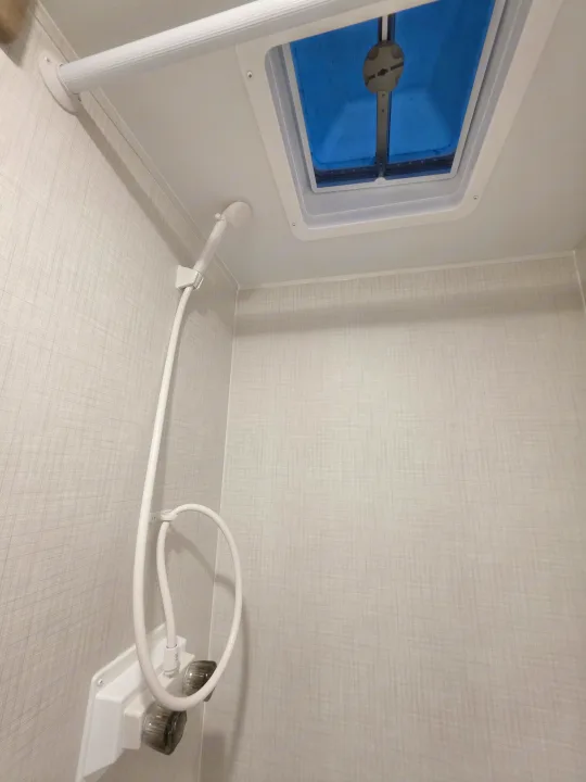 Inside an RV rental: a compact bathroom with a white shower head, water controls, and a blue-tinted ceiling skylight.. Keystone Springdale 2026