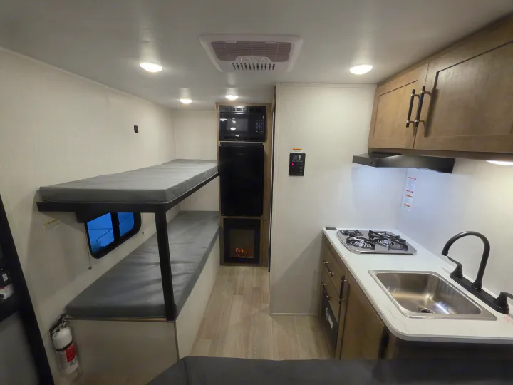 Inside this rv rental: practical bunk beds, a compact kitchen with stove, sink, microwave, and mini-fridge, all in a modern setting.. Keystone Springdale 2026