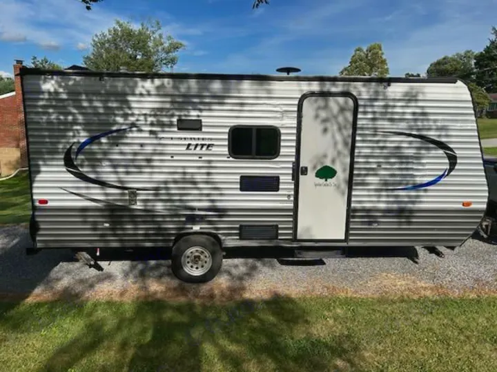 This light-colored travel trailer RV rental features horizontal siding, blue/black decals, and a green tree logo on its door.. Crossroads RV Z-1 Lite 2017