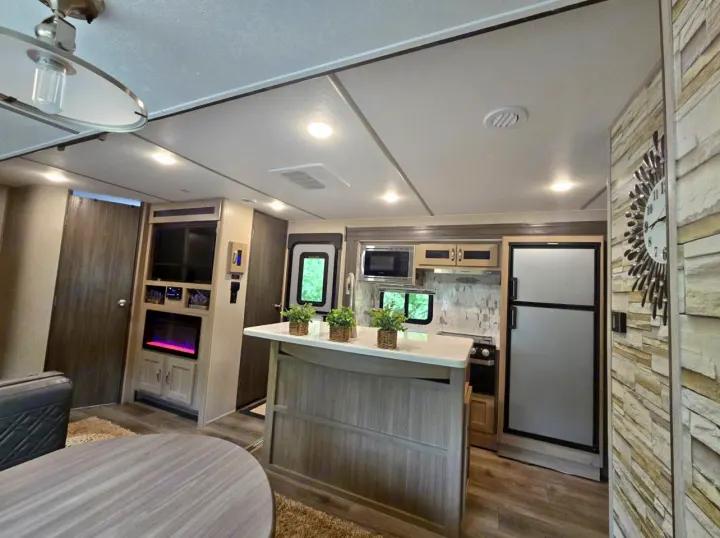 Inside a modern RV rental: spacious living area with fireplace, well-equipped kitchen island, and large refrigerator.. Coachmen Forest River Freedom Express Liberty Series M-320 BHDS 2021