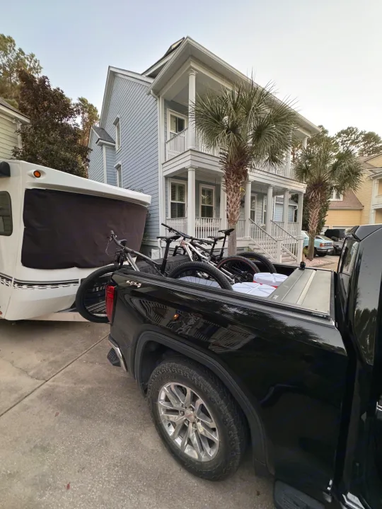 A black pickup truck with bikes and coolers hitches to a white travel trailer RV rental near a blue house.. InTech RV Sol 2023