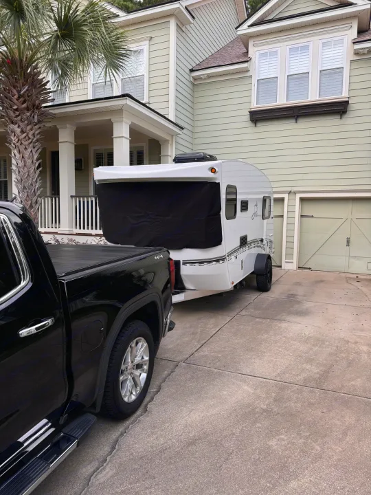 Preparing for an outdoor adventure: a black pickup truck hitched to a compact RV rental in a driveway.. InTech RV Sol 2023
