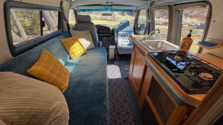 Interior of a comfortable rv rental with kitchen, spacious seating, and large windows revealing the outdoors.. Coachmen Van Conversion 1994