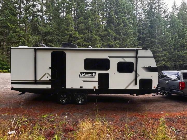 A white Coleman travel trailer is hitched to a Ford Ranger truck, ideal for an RV rental camping trip in the forest.. Keystone Coleman Light 2026
