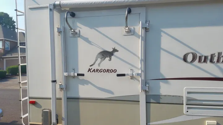 Side view of an RV rental with a "Kargoroo" decal on its door, ladder, and awning overhead. Ready for travel.. Keystone RV Outback Sydney 2007