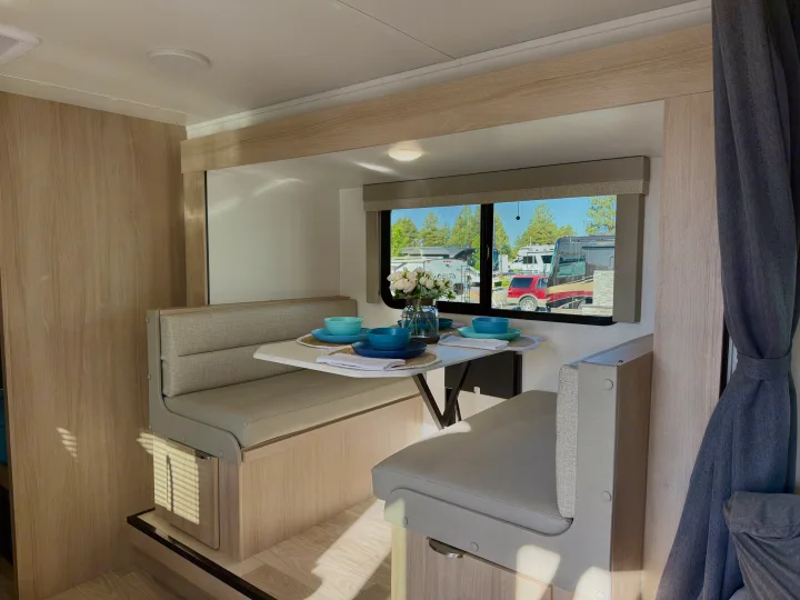 Bright rv rental interior: A comfortable dining area with bench seating, set table, and a large window view.. Winnebago Micro Minnie 2025