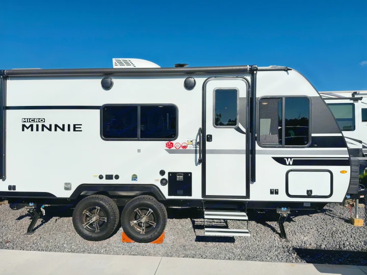 White Winnebago Micro Minnie travel trailer, ideal for your next RV rental adventure, parked on gravel under a blue sky.. Winnebago Micro Minnie 2025