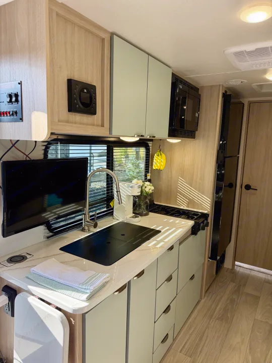 Bright rv rental interior featuring a compact kitchen: sink, stove, microwave, TV, and stylish light wood finishes.. Winnebago Micro Minnie 2025