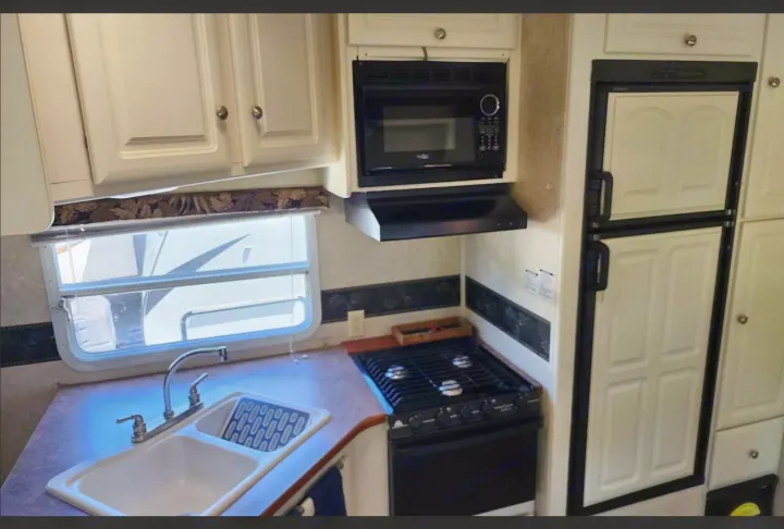 Well-equipped RV rental kitchen with sink, stove, microwave, refrigerator, and ample storage cabinets.. Keystone RV Outback Sydney 2007