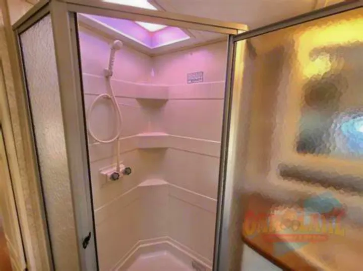 This rv rental features a compact, white corner shower unit with a handheld sprayer and skylight, ideal for travel.. Keystone RV Outback Sydney 2007