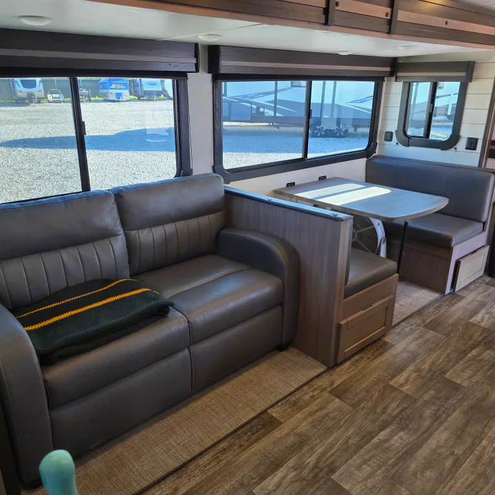 RV rental interior: spacious living area with dark gray sofa, dinette, and large windows showing outdoor RVs.. Crossroads RV Sunset Trail Super Lite 2022
