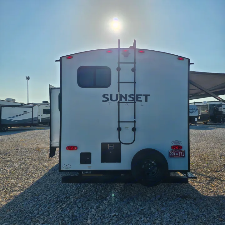 This Sunset Trail RV rental, parked on a gravel lot, shows its rear ladder, spare tire, and Oklahoma plate PPK 771.. Crossroads RV Sunset Trail Super Lite 2022