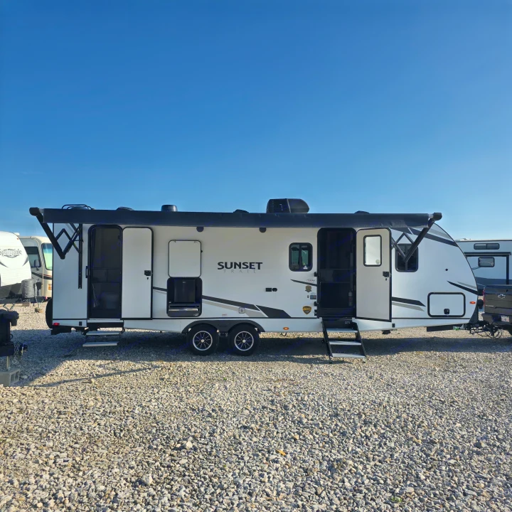 This white Sunset Trail RV rental, with its doors open and awning extended on a gravel lot, is ready for your next adventure under a clear blue sky.. Crossroads RV Sunset Trail Super Lite 2022
