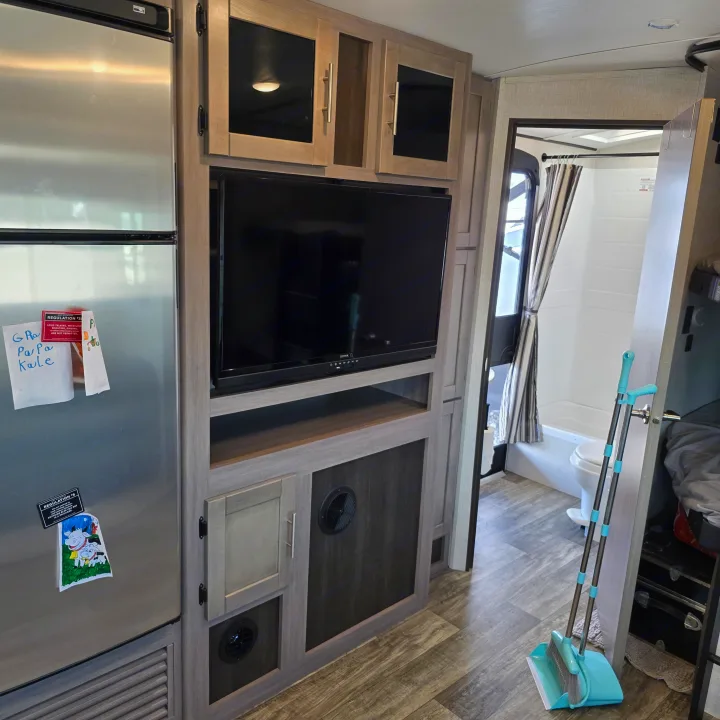 Compact RV rental interior featuring a kitchen with fridge, living area with TV, and a glimpse of the compact bathroom.. Crossroads RV Sunset Trail Super Lite 2022