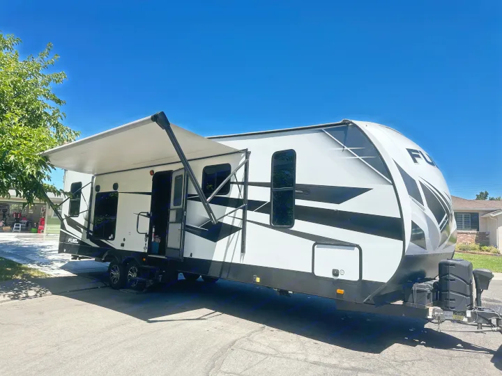 Modern white and black travel trailer RV rental with awning extended, parked on a sunny day.. Heartland Fuel 287 2022