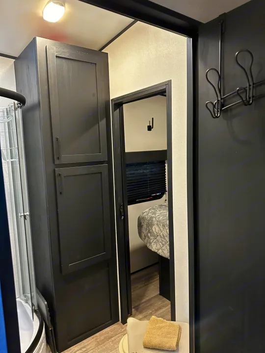 RV rental interior shows a compact bathroom with shower, toilet, storage cabinet, and a view into the bedroom.. Heartland Fuel 287 2022