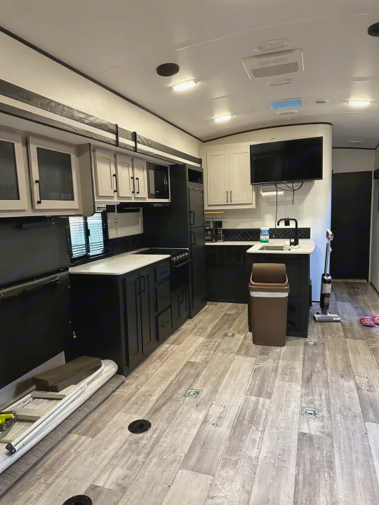Inside a modern RV rental: light and dark kitchen cabinets, TV, wood-look floor. Features include a sink, stove, and fridge.. Heartland Fuel 287 2022