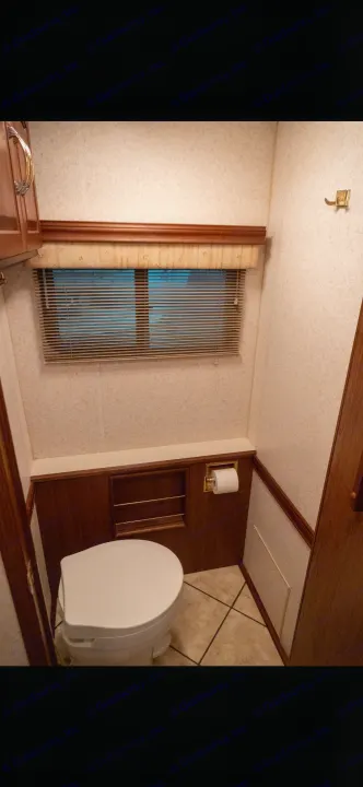 Compact RV rental bathroom features a toilet, small window with blinds, and practical wood details.. Itasca Horizon 2002