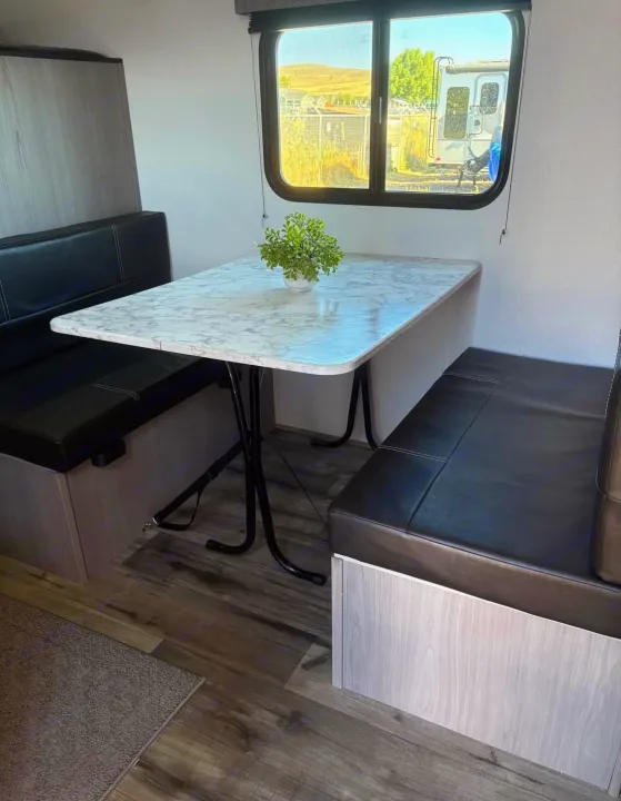 Inside an RV rental: a bright dinette features black upholstered benches, a white marble-patterned table, and scenic window views.. Dutchmen Other 2024