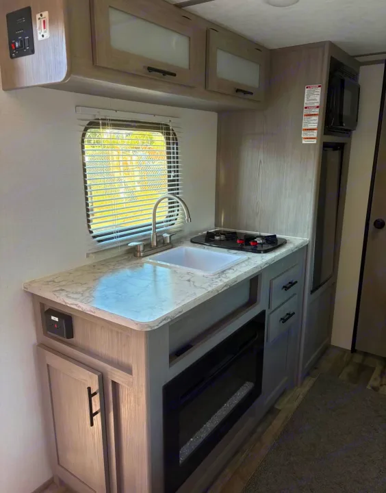 RV rental: Modern kitchen with sink, stove, and fireplace. Light wood cabinets in this functional camper.. Dutchmen Other 2024