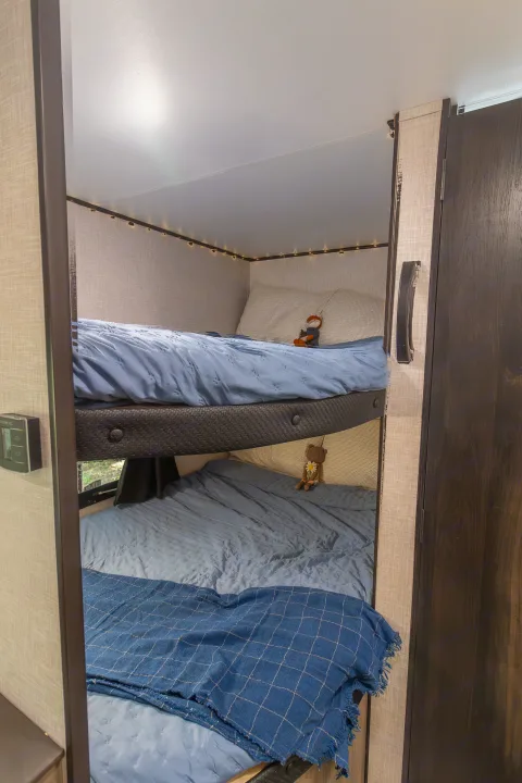 Cozy RV rental features two stacked bunk beds with blue bedding, complete with cute stuffed animals. A comfortable sleeping area.. Jayco Jay Flight SLX 2024