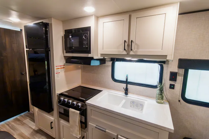 RV rental kitchen: black refrigerator, microwave, stove, white sink, light cabinets, and wood flooring.. Jayco Jay Flight SLX 2024
