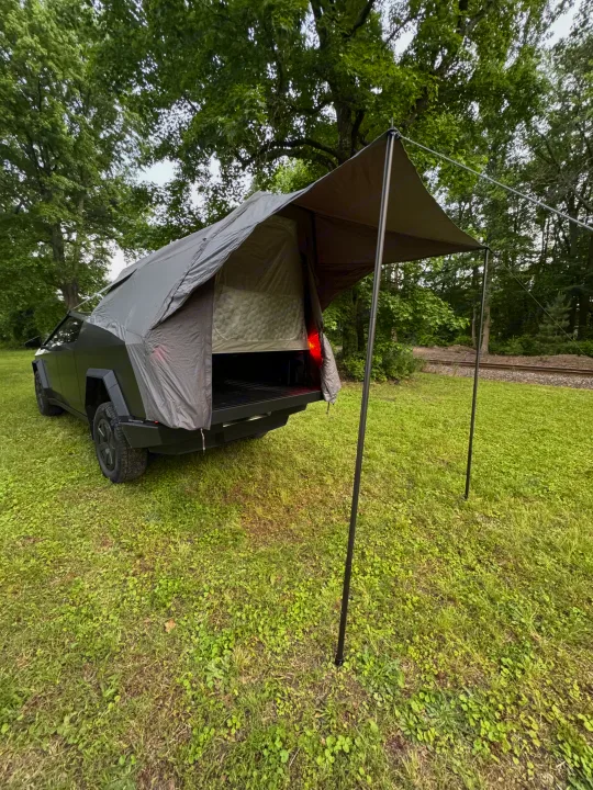 Innovative Cybertruck camping setup, potentially for an RV rental, with a rear tent and awning in a grassy field.. Tesla Cybertruck 2025