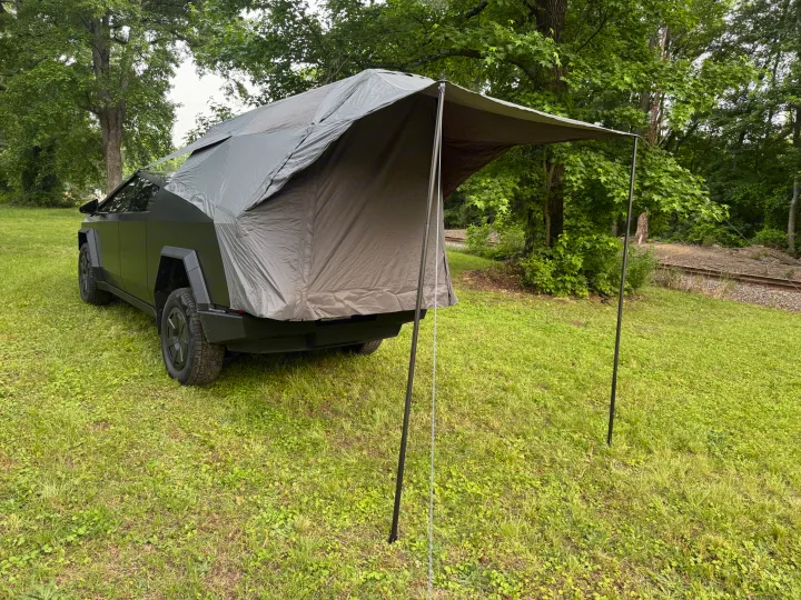 Dark grey Tesla Cybertruck with an attached rear tent, parked on grass. A unique RV rental option for outdoor adventure.. Tesla Cybertruck 2025