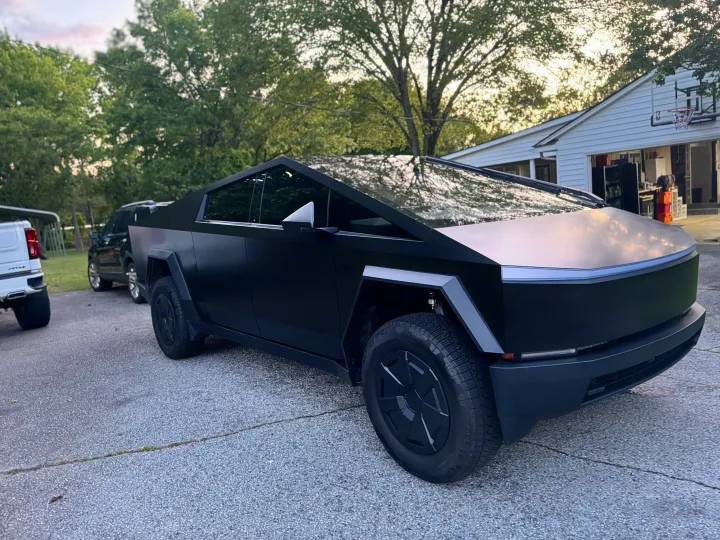 A matte black Tesla Cybertruck with a white pickup & SUV on a driveway. Great for a road trip, or an RV rental.. Tesla Cybertruck 2025