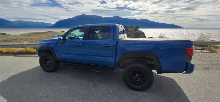 A blue pickup truck parked by a vast lake & snowy mountains. Great for road trips! Think about an rv rental for more space.. toyota Tacoma 2018