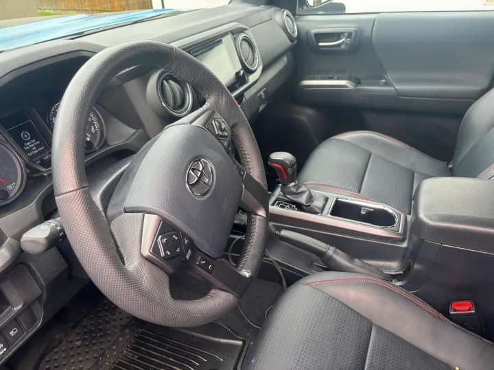 Driver's view inside a modern car, featuring the detailed steering wheel, dashboard, gear shifter, and black seats. Ideal for an RV rental trip.. toyota Tacoma 2018