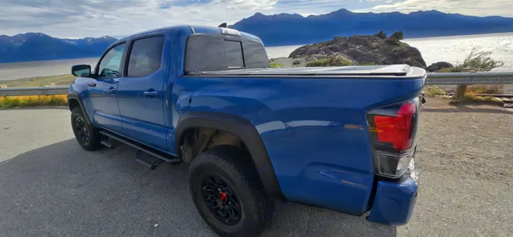 A blue pickup truck, ideal for adventures or an rv rental alternative, parked by a scenic lake with distant mountains.. toyota Tacoma 2018