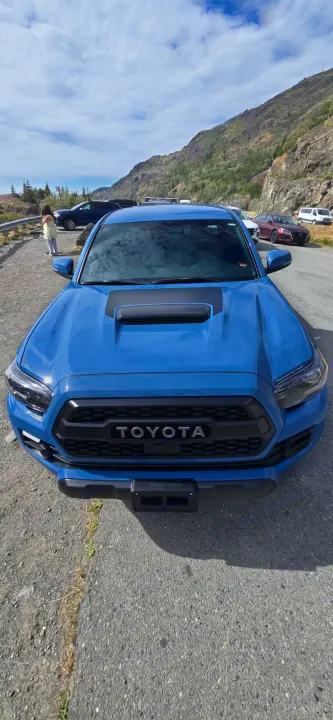 A bright blue Toyota Tacoma truck parked on a mountain road with other vehicles, including a white RV rental in the distance.. toyota Tacoma 2018