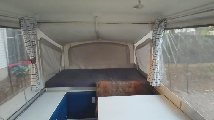 Inside an RV rental: a large bed, dining table, and plaid curtains define this pop-up camper's inviting interior.. Coleman Destiny Santa Fe 1996