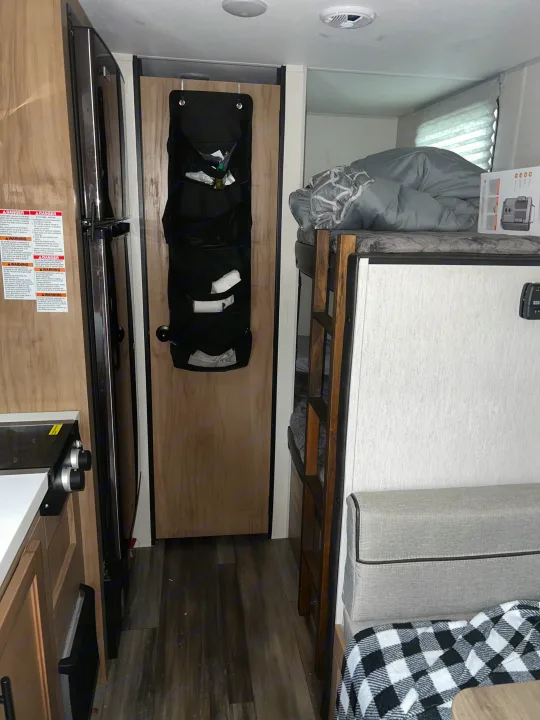 This RV rental interior features a kitchen area on the left, a refrigerator, door storage, and bunk beds on the right in a compact layout.. Forest River Cherokee Wolf Pup 2023