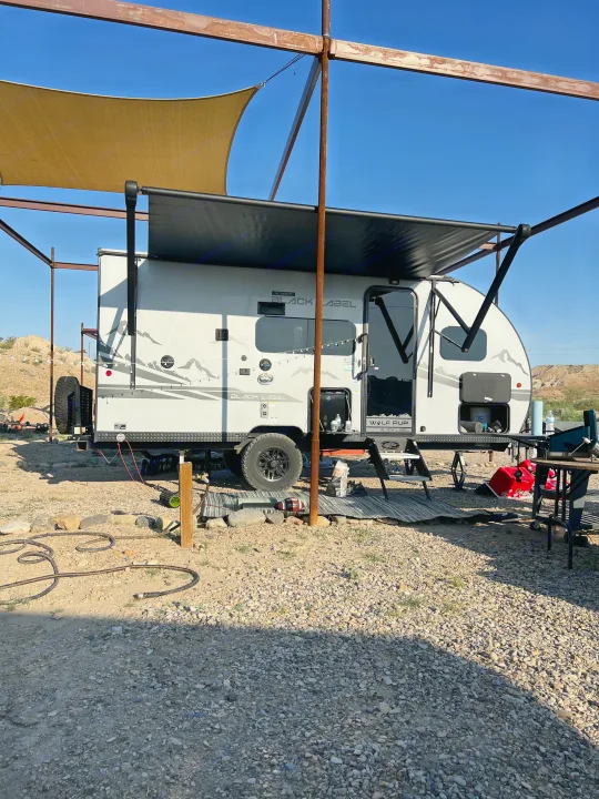 RV rental travel trailer set up at a sunny desert campsite with extended awning under a metal shade structure.. Forest River Cherokee Wolf Pup 2023