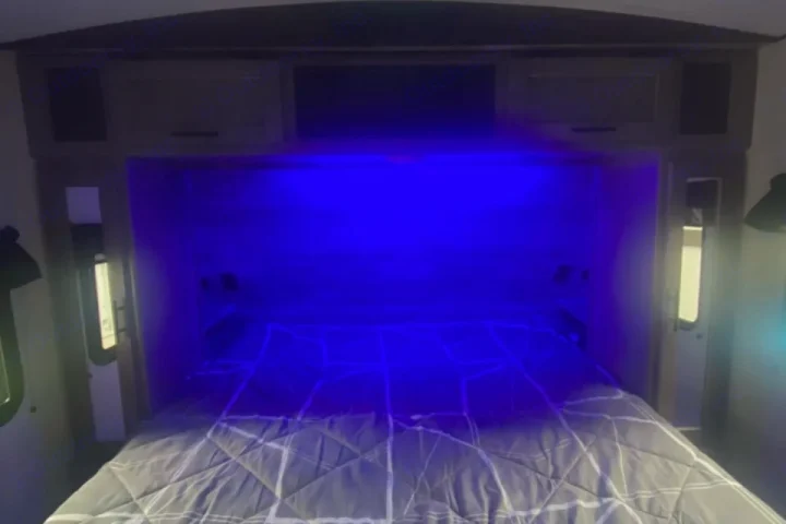 Cozy RV rental bedroom with a gray patterned bed, illuminated by a vibrant blue LED light above the headboard.. Crossroads RV Sunset Trail Super Lite 2023