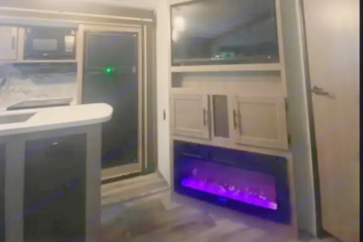 This RV rental interior features a kitchen with microwave and fridge, along with a living area showcasing a TV and glowing purple fireplace.. Crossroads RV Sunset Trail Super Lite 2023