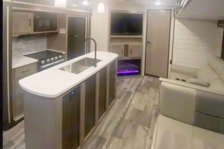Modern RV rental interior with a fully equipped kitchen island, living area sofa, TV, and glowing electric fireplace.. Crossroads RV Sunset Trail Super Lite 2023