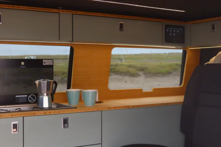 Compact RV rental kitchen features a Moka pot, Dometic hob, sleek storage, smart controls, and scenic window views.. Volkswagen Transporter 2023