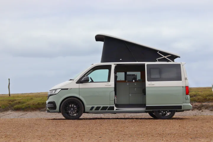 Two-tone camper van with pop-top roof & open door revealing interior, on a dirt road; perfect for rv rental.. Volkswagen Transporter 2023
