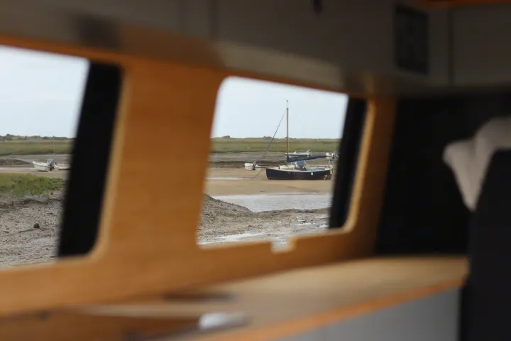 Serene view from an RV rental: boats resting on a tidal flat, seen through the camper's window. Peaceful waterside escape.. Volkswagen Transporter 2023